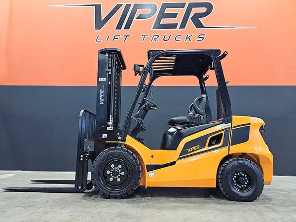 A yellow and black forklift parked in front of an orange wall.