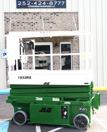 A green scissor lift parked in front of a building.