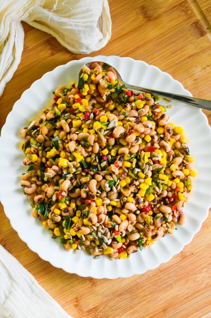 marinated black eyed pea salad with corn, collard greens, bell peppers, and sunflowers seeds served on a white scalloped plate.
