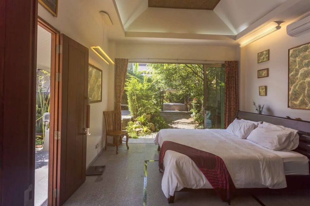 Hotel room interior with a bed near a large glass door leading to a garden