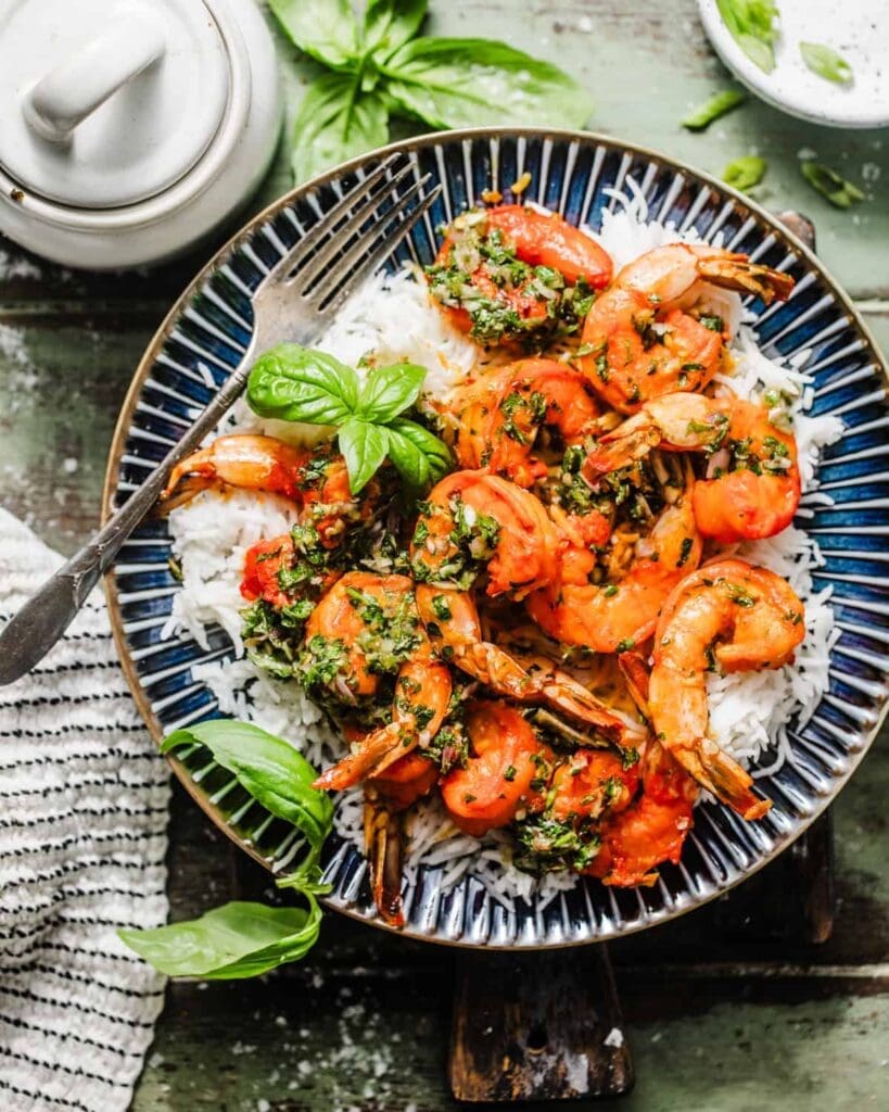 shrimp chimichurri on a plate on top of white rice and topped with fresh basil.