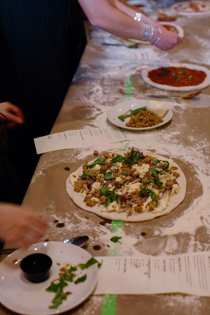 People preparing homemade pizzas with toppings.