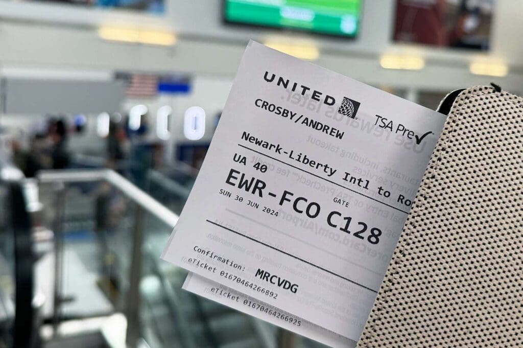 A United boarding pass for a flight from Newark to Rome being held with an airport terminal background