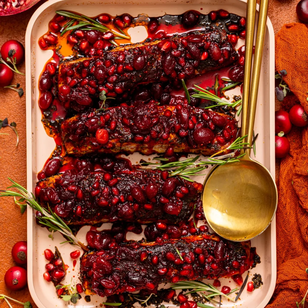Baked Christmas Salmon with Cranberry-Pomegranate Glaze on a griddle pan with serving spoons.