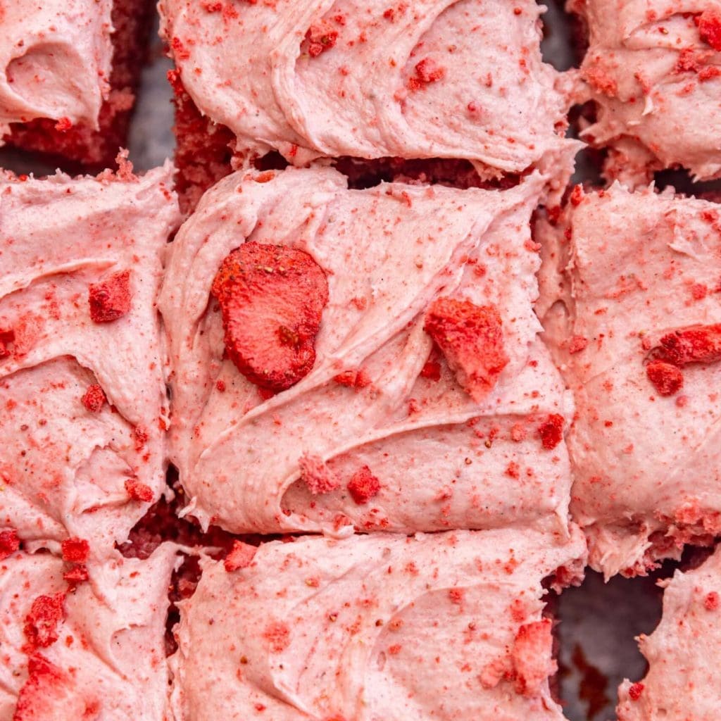 Close up of strawberry cream cheese frosting on top of a cake with chopped freeze dried strawberries sprinkled on top.